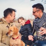 LGBT fostering. two fathers and their foster daughter on a walk with their dog